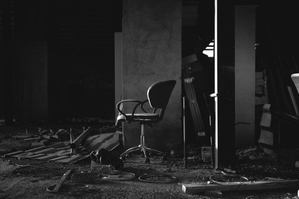 Black and white photo of an office chair amid debris, concrete walls