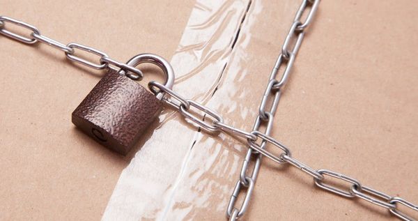 Rusted padlock secured with interlocking metal chains against a beige textured background, symbolizing protection
