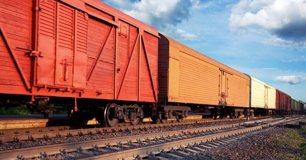 Cargo train with red and yellow boxcars rolling on railroad tracks under a blue sky with fluffy clouds