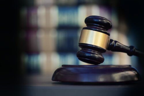 Dark wooden gavel with gold accent resting on matching sound block, blurred legal library background in soft focus