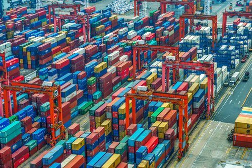 Aerial view of bustling cargo shipping port with colorful stacked shipping containers and red gantry