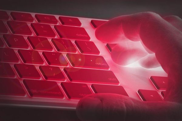 A hand hovers over a red-tinted keyboard featuring a glowing light effect emphasizing the delete and return keys