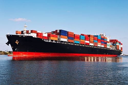Large cargo ship loaded with colorful shipping containers, sailing on calm blue water with a clear sky