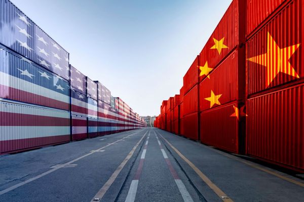 Shipping containers with US and Chinese flags line a road, symbolizing trade tensions and economic conflict