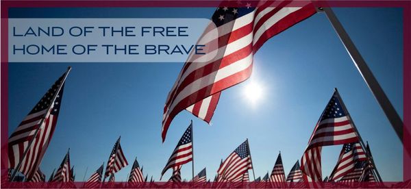 Multiple American flags wave against a bright blue sky