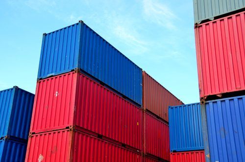 Stacked shipping containers in blue and red, neatly arranged against a clear blue sky, showcasing industrial