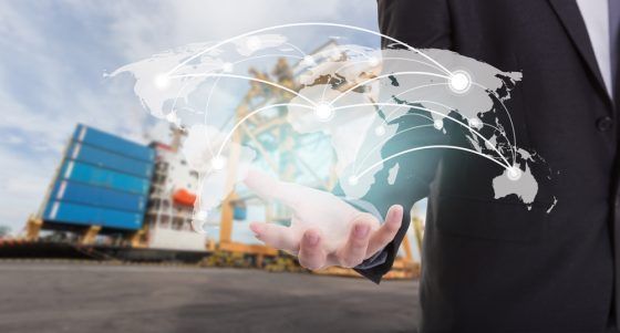 Businessman's hand holding a holographic world map with connected network lines, industrial shipping containers
