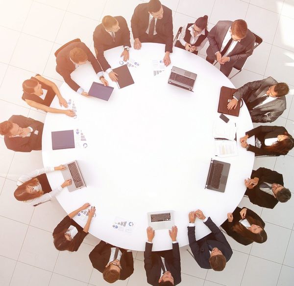 Business team gathered around a circular white table with laptops, documents, and graphs, viewed from overhead