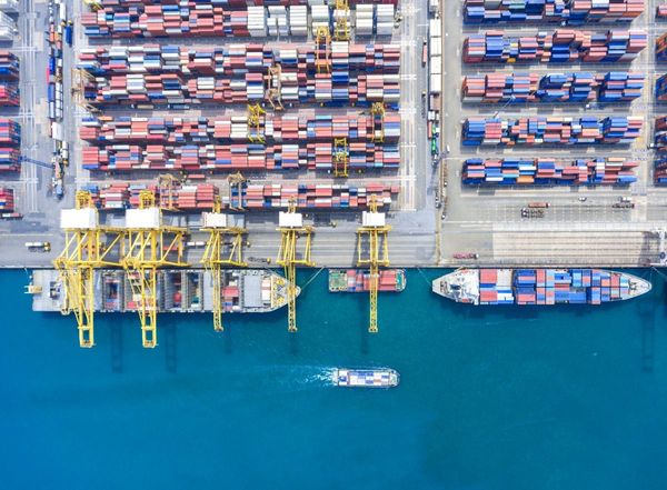 Aerial view of a bustling shipping port with yellow cranes, stacked colorful cargo containers, and container ships