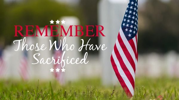 A red and white text "remember those who have sacrificed" next to an american flag on grass
