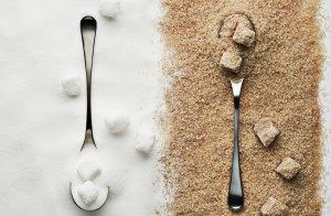 Two silver spoons, one on white surface with white sugar cubes, and the other on brown sugar background with brown sugar cubes