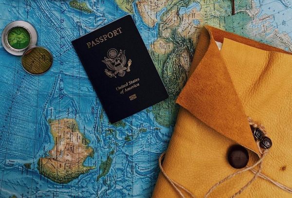 A US passport rests on a blue world map beside a compass and a yellow leather travel wallet tied with twine