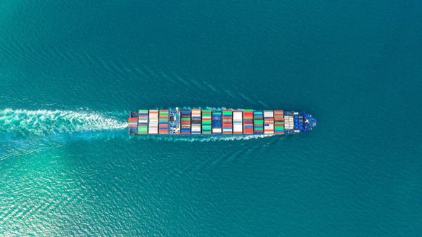 Aerial view of a large container ship sailing through turquoise ocean waters, laden with colorful shipping