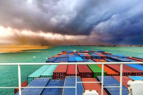 Colorful cargo containers stacked on ship deck with dramatic stormy sky and turquoise ocean horizon in background