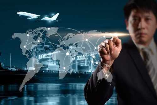 Businessman touches glowing world map with shipping routes, airplane, and cargo vessels in blue-tinted global