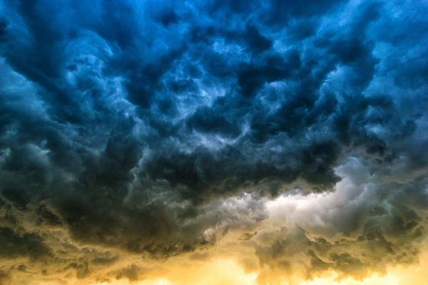 Dramatic stormy sky with swirling dark blue clouds transitioning to golden yellow at the horizon
