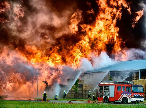 Firefighters battle massive orange and yellow flames engulfing a building featuring a red fire truck spraying water