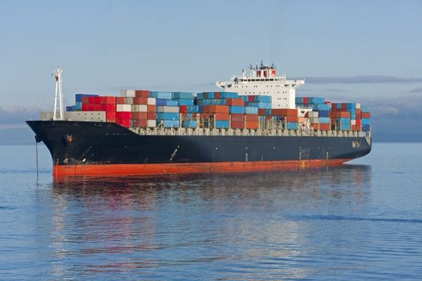 Massive cargo ship loaded with colorful shipping containers, floating on calm blue waters with a misty horizon