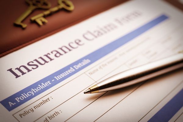 Blank insurance claim form with ballpoint pen and two antique brass keys, symbolizing policy coverage and protection