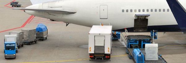 White passenger aircraft on tarmac with blue service vehicles and cargo loaders preparing for departure or arrival