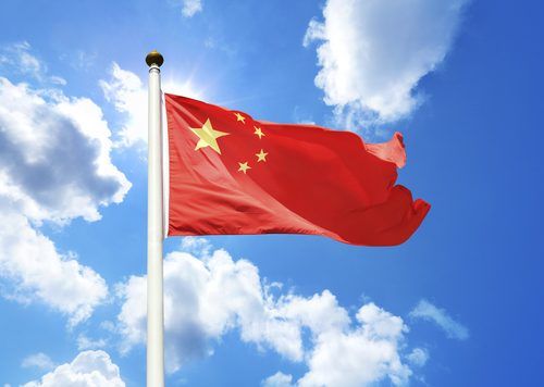 Chinese national flag waving against a bright blue sky with white fluffy clouds
