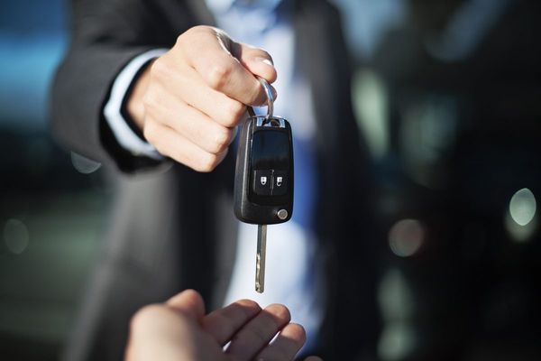 Car key being handed over from one suited hand to another against a blurred office background
