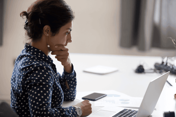 Businesswoman in polka dot blouse reviewing documents and laptop at office desk