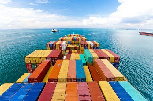 Colorful shipping containers stacked on a cargo ship's deck, sailing across a calm blue ocean under a cloudy sky