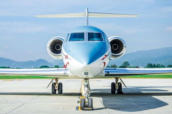 Private jet with sleek blue and white fuselage parked on tarmac, two jet engines, mountainous landscape in background