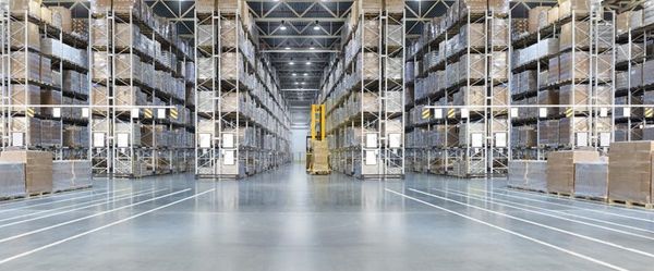 Symmetrical warehouse interior with tall metal shelving units, stacked boxes, and a yellow forklift down a central