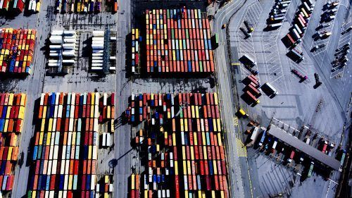 Aerial view of dense shipping container yard with multicolored rectangular containers stacked in organized rows