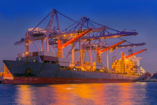 Massive cargo ship loaded with colorful shipping containers, illuminated by golden light at dusk with large cranes