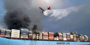 Fire-fighting aircraft sprays water on burning Maersk cargo container ship with thick black smoke billowing