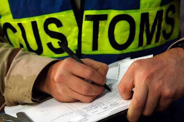 Customs officer in high-visibility vest fills out paperwork with a pen, focusing on the document in front of them