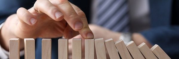 A hand stopping a chain reaction of wooden domino blocks from falling, symbolizing risk management or prevention