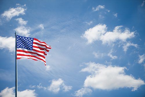 American flag waving against a bright blue sky with white fluffy clouds
